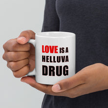 Load image into Gallery viewer, 11oz white ceramic mug with the caption 'love is a helluva drug' in black and red letters
