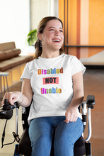 Load image into Gallery viewer, Smiling woman in a wheelchair wearing a white unisex t-shirt stating 'Disabled NOT Unable' in multi-colored letters
