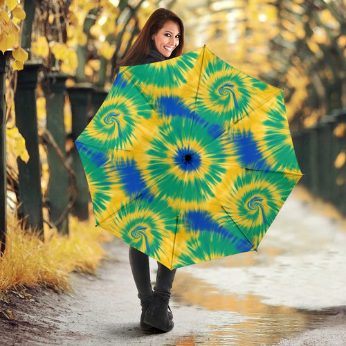 Person holding a large tie-dye spiral pattern umbrella in blue, yellow and green spirals
