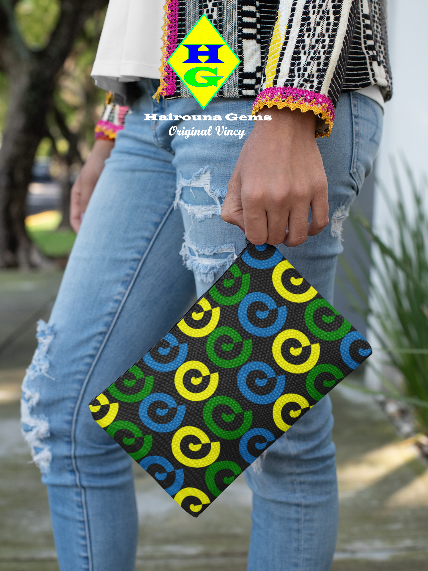 Black pouch with blue, yellow and green spirals being held by a woman on the street viewed from the waist down.