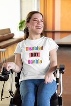 Load image into Gallery viewer, Smiling woman in a wheelchair wearing a white unisex t-shirt stating &#39;Disabled NOT Unable&#39; in multi-colored letters
