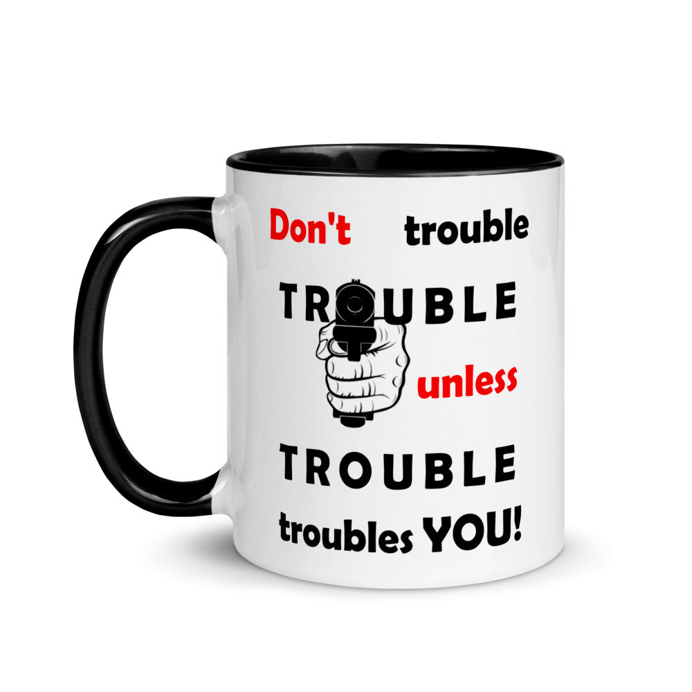 White ceramic mug with black painted on the  handle and inside sporting the  motto 'don't trouble trouble unless trouble troubles you' in black and red letters and a hand holding a gun.